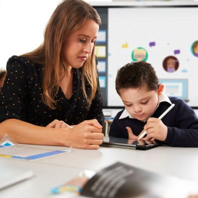 A special education teacher working one-on-one with a student on a tablet.