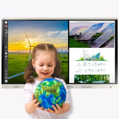 A young girl smiling while holding a globe with illustrations of greenery and water, with a SMART Board displays in the background showing renewable energy themes, one with wind turbines at sunset and another with solar and wind power infographics.