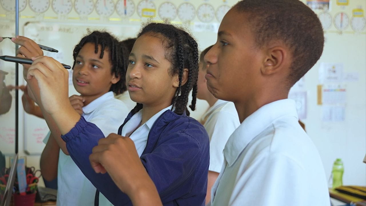 Vera School students actively participating in a class using a SMART board, enhancing their learning experience with technology.