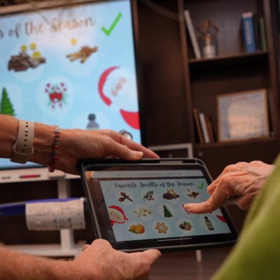 A senior care resident's hand, interacting with a tablet that is reflected on a SMART Display.