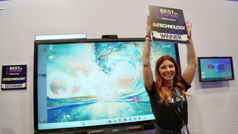 SMART representative, Jessica Secan, holding up the ‘Winner” sign in front of the SMART Board QX Pro at InfoComm.