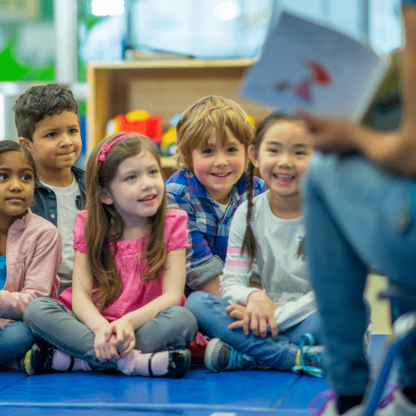 5 Kindergarten students sitting and listening to their teacher who is out of focus. 